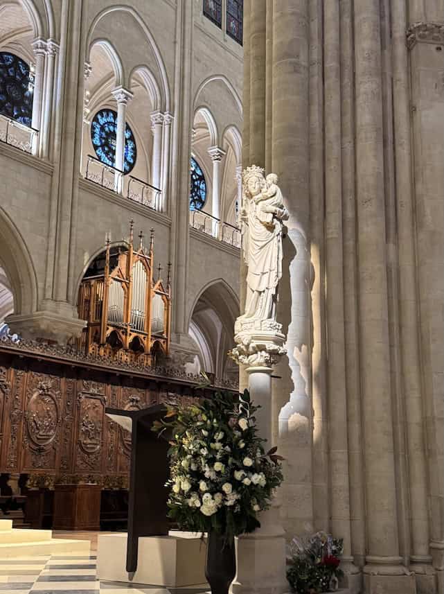 Notre Dame de Paris statue of Our Lady holding baby Jesus displayed at the side of the front altar with a spotlight shining on her