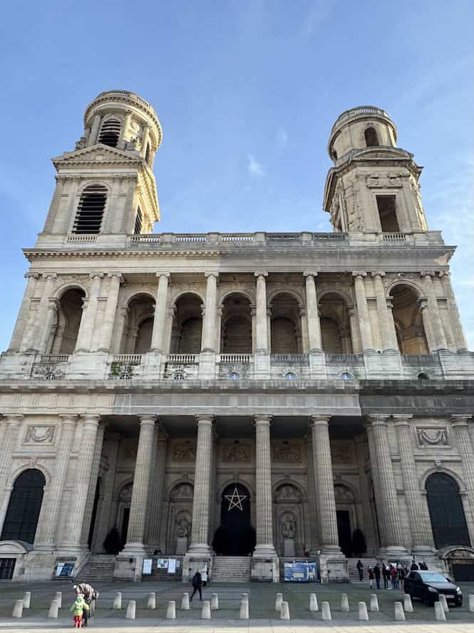Exterior of St. Sulpice Catholic Church in Paris, France with two asymetrical bell towers extending up into the blue skies above