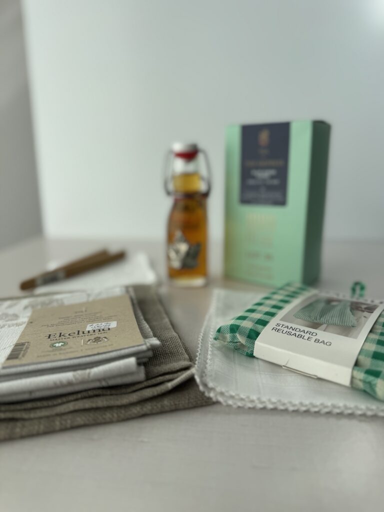 Souvenirs from Victoria, BC on a table including linen tea towels, reusable bag, maple syrup in a swig top bottle, and a box of tea in the background.