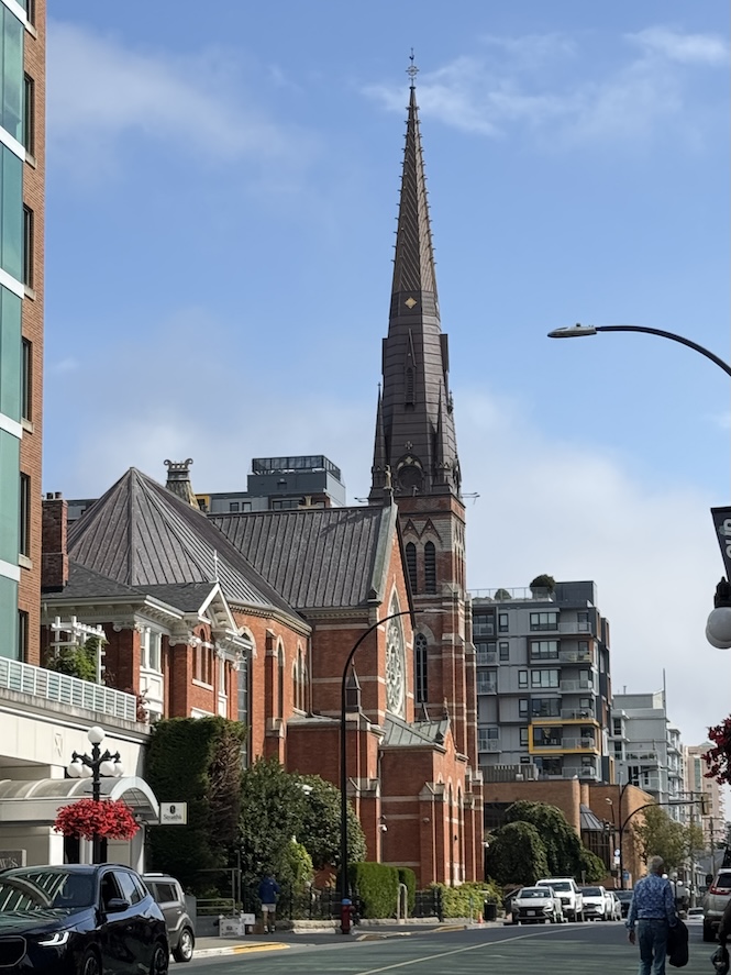 The side angle of the exterior of St. Andrew's Cathedral in Victoria, BC on a day with blue skies and light clouds, it's stark red bricks stand out with the sun shining on it