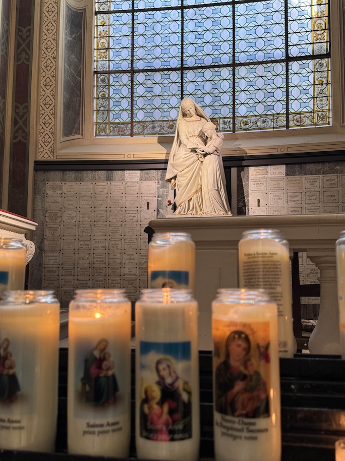 Ex votos line the church wall around the altar and statue of St. Anne tenderly instructing Mary. In the foreground, candles lit in honor of St Anne