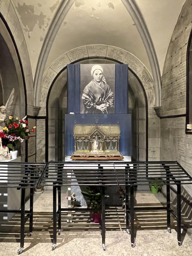 Chapel dedicated to St. Bernadette's relic with a picture of St. Bernadette on the top and right below is the reliquary in the shape of a chapel adorned with images of her and Our Lady
