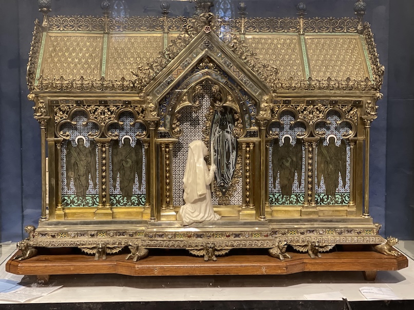 Reliquary of St. Bernadette made of brass in the shape of a chapel adorned with decorations of St. Bernadette and Our Lady of Lourdes and angels in the windows