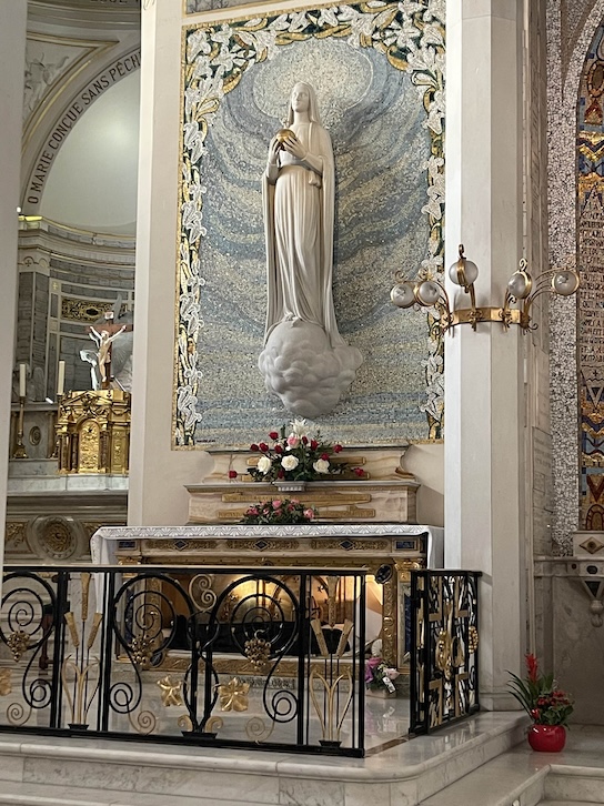 The uncorrupt body of St Catherine Laboure rests under a side altar, above a statue of Mary with a mosaic behind