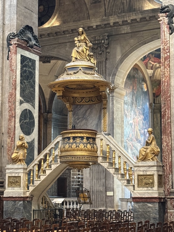 A beautiful baroque pulpit with two stairs leading up to it flanked by statues inside a grandiose church
