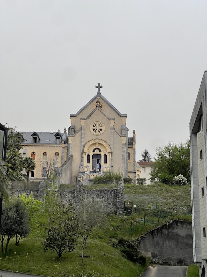 The exterior of the Chapelle de L'Hospitalet as seen walking up from the Sanctuary of Lourdes: stairs lead up to the side of a church