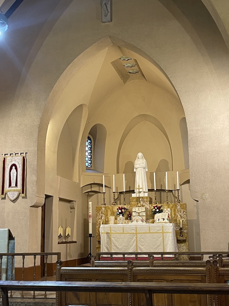 A traditional catholic altart adorned for Mass in the Chapelle de L'Hospitalet, Lourdes, France. The altar is in an alcove with a statue of Mary above the altar flanked by three candles on both sides.