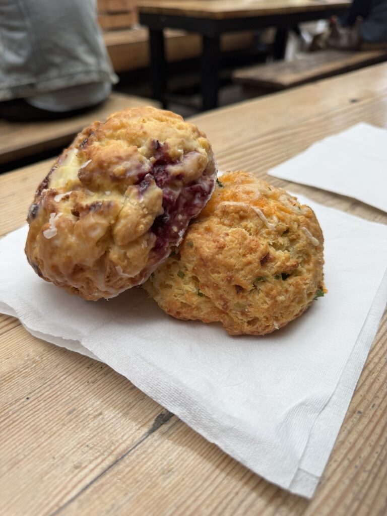 Two large round scones arranged on a napkin with the top one containing raspberry and white chocolate and the bottom one containing cheddar and onions