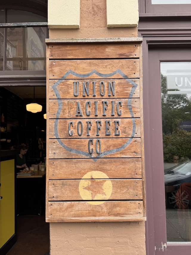 Union Pacific Coffee Co written in metal is attached onto a sign made up of horizontal wooden planks, under the words is a star inside of a circle symbol