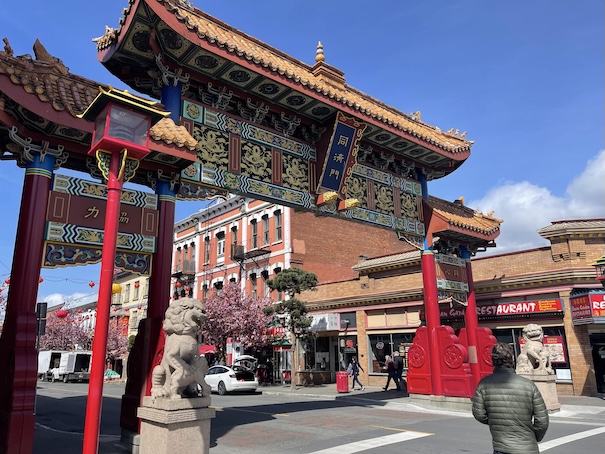 A chinese architectural arch or gate is erected over a street in Victoria, BC with a red lantern street light in front of it on the sidewalk