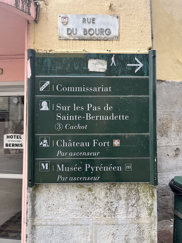A green street sign against a wall in Lourdes' rue du bourg