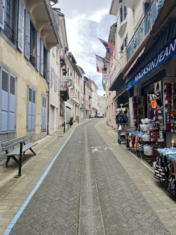 A walking street in Lourdes with the path of St Bernadette in a blue line down the street. On the right a catholic shop under two flags.
