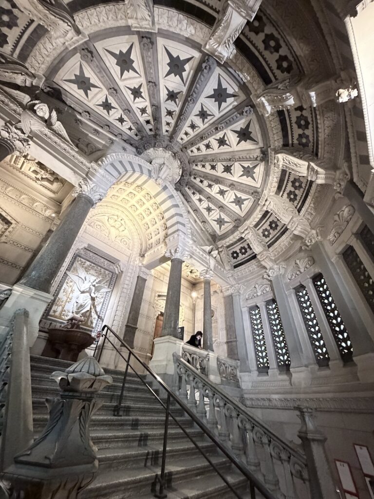 Ornate staircase and domed ceiling inside the crypt of the Basilica of Notre-Dame de Fourvière in Lyon, France.
