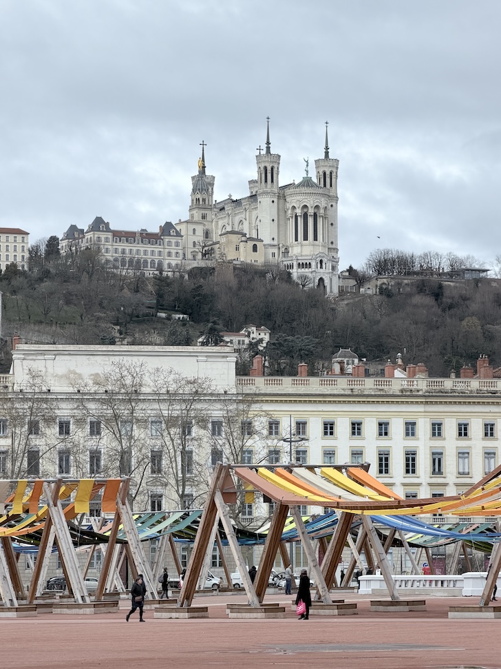 Place Bellecour in Lyon with colorful installation and the Basilica of Notre-Dame de Fourvière on the hilltop.