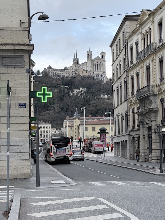 City street in Lyon with Basilica of Notre-Dame de Fourvière visible on the hilltop in the background.
