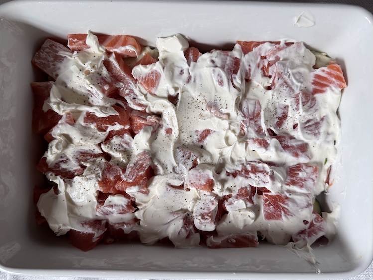 Crème fraîche cream spread smoothly over a layer of fresh salmon cubes and seasoned with cracked black pepper.