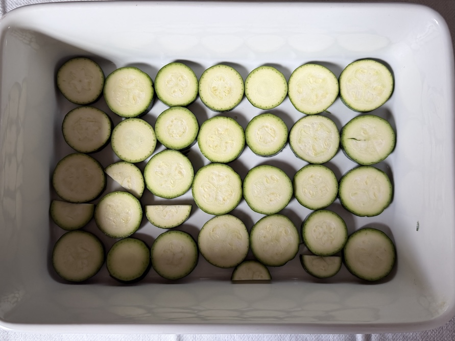 A single layer of sliced zucchini rounds in a white rectangle ceramic baking dish