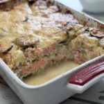 A side-profile slice of a salmon zucchini gratin showing layers of pink salmon, green zucchini rounds, and creamy sauce.