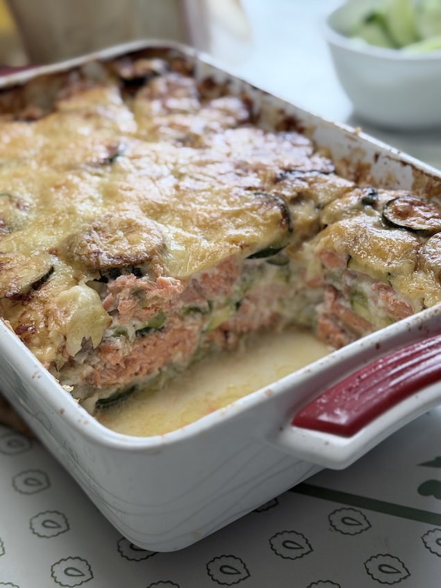 A side-profile slice of a salmon zucchini gratin showing layers of pink salmon, green zucchini rounds, and creamy sauce.