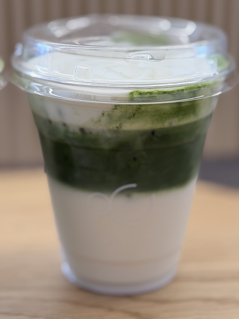 Close-up of a layered iced matcha latte featuring cold milk and dark green freshly milled matcha in a clear plastic cup.