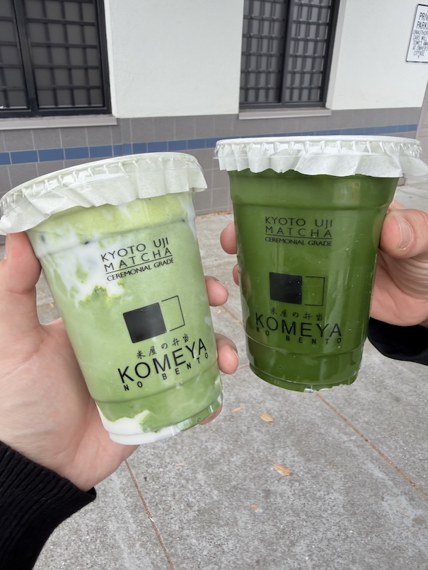 Two hands holding iced Japanese green tea drinks from Komeya No Bento, including a creamy iced matcha latte and a pure iced matcha.