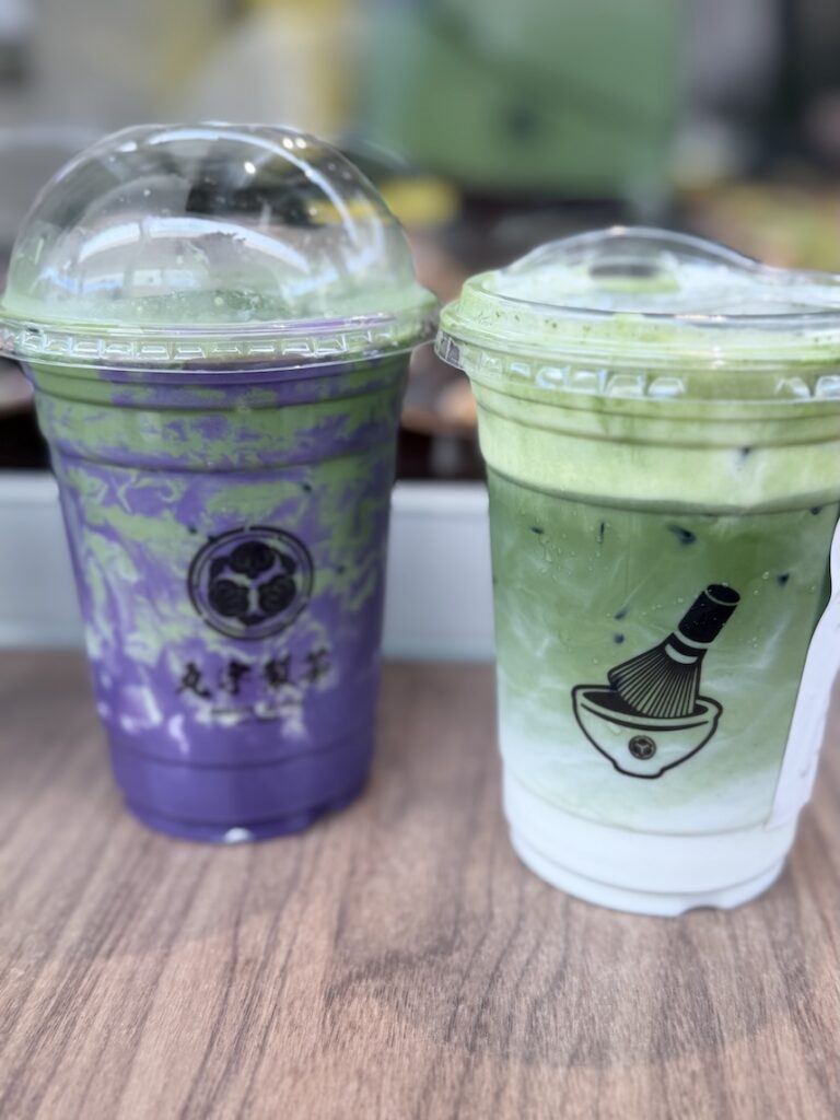 Two iced matcha lattes from Maruwu Seicha, including a purple ube matcha latte and a classic layered matcha latte with foam.