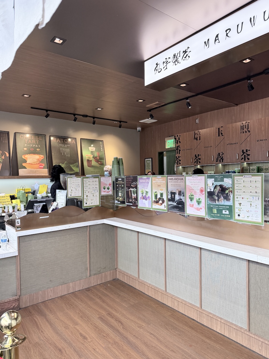 Interior ordering counter at Maruwu Seicha tea shop in Japantown San Francisco, featuring illuminated brand signage, drink posters, and Japanese tea displays.