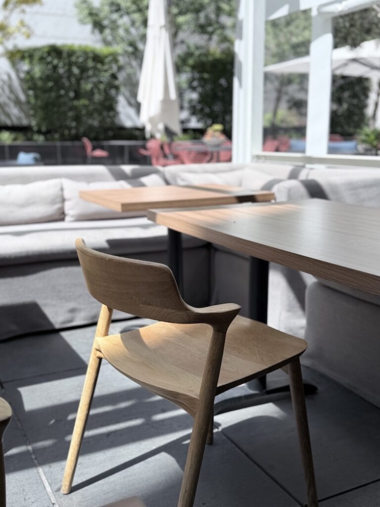 Sunlit outdoor patio seating at Shoji in San Francisco featuring wooden chairs, light-colored cushioned bench seats, and wooden tables.